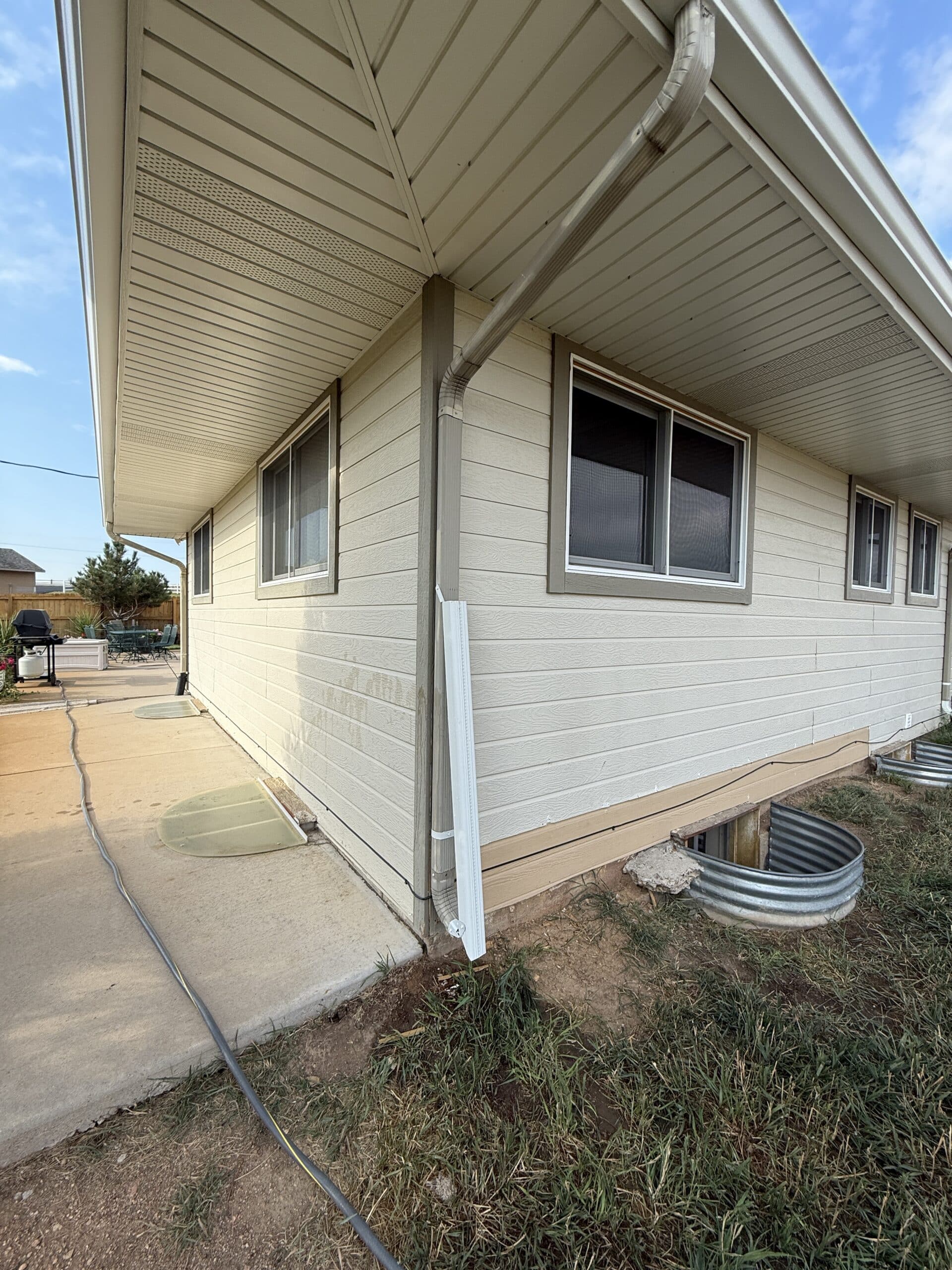 Side view of a residential home exterior featuring light beige siding, multiple windows, and a downspout.