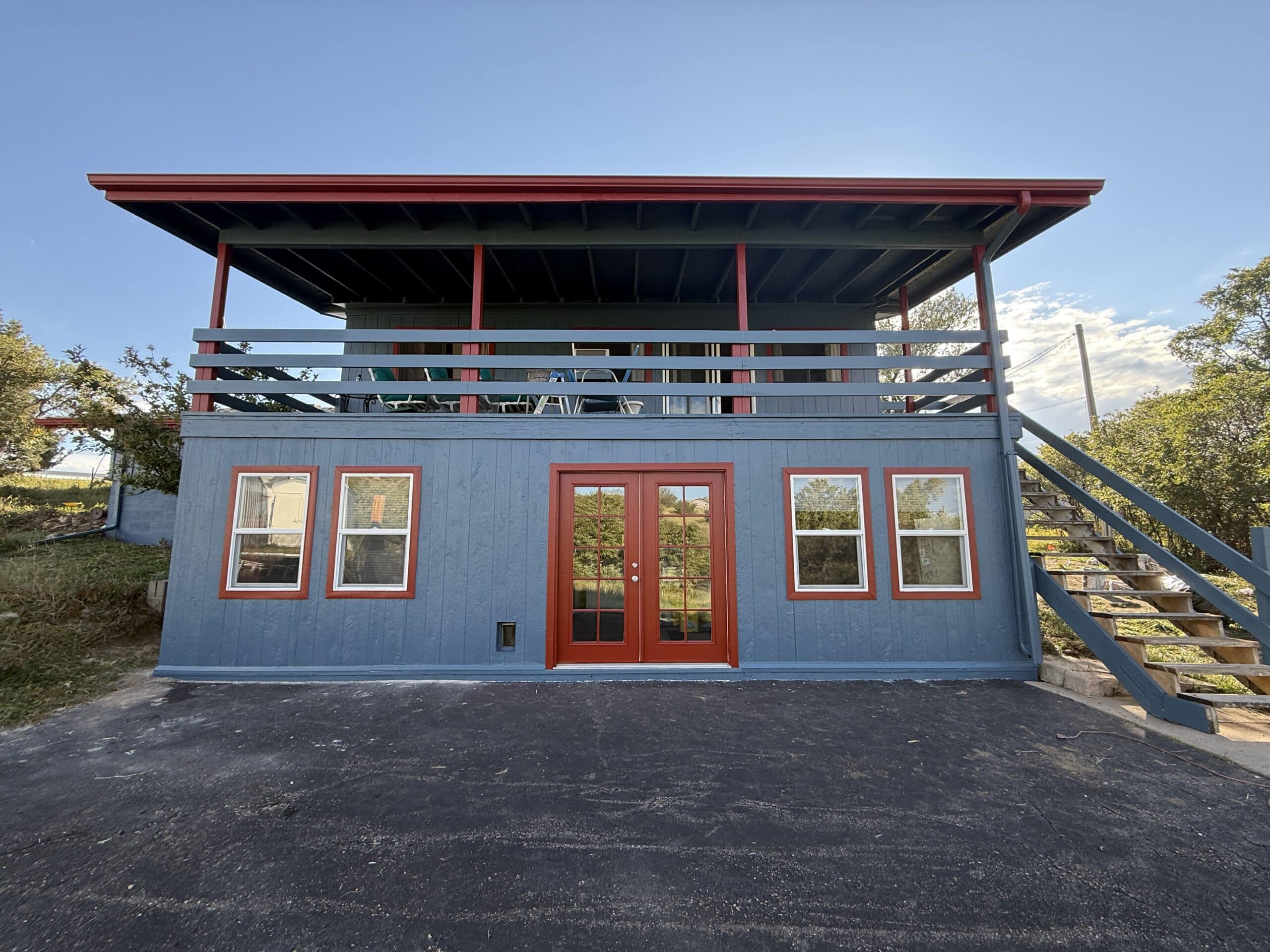Front view of a beautifully completed blue house with red trim and double doors, showcasing exterior painting.