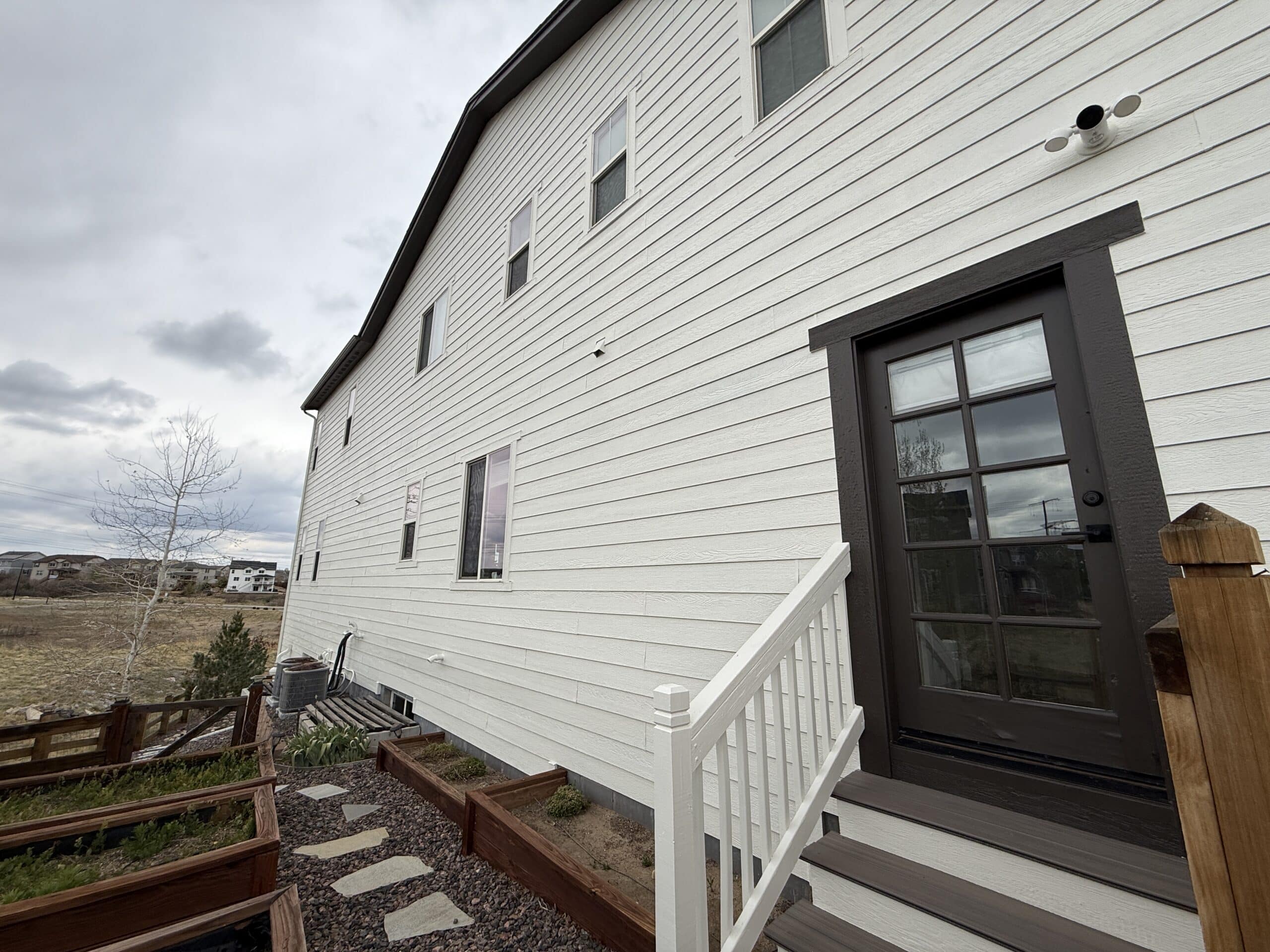 Professional Exterior House Painting with White Siding and Dark Door Freshly painted white exterior house siding with a dark brown door and steps, highlighting quality residential painting.