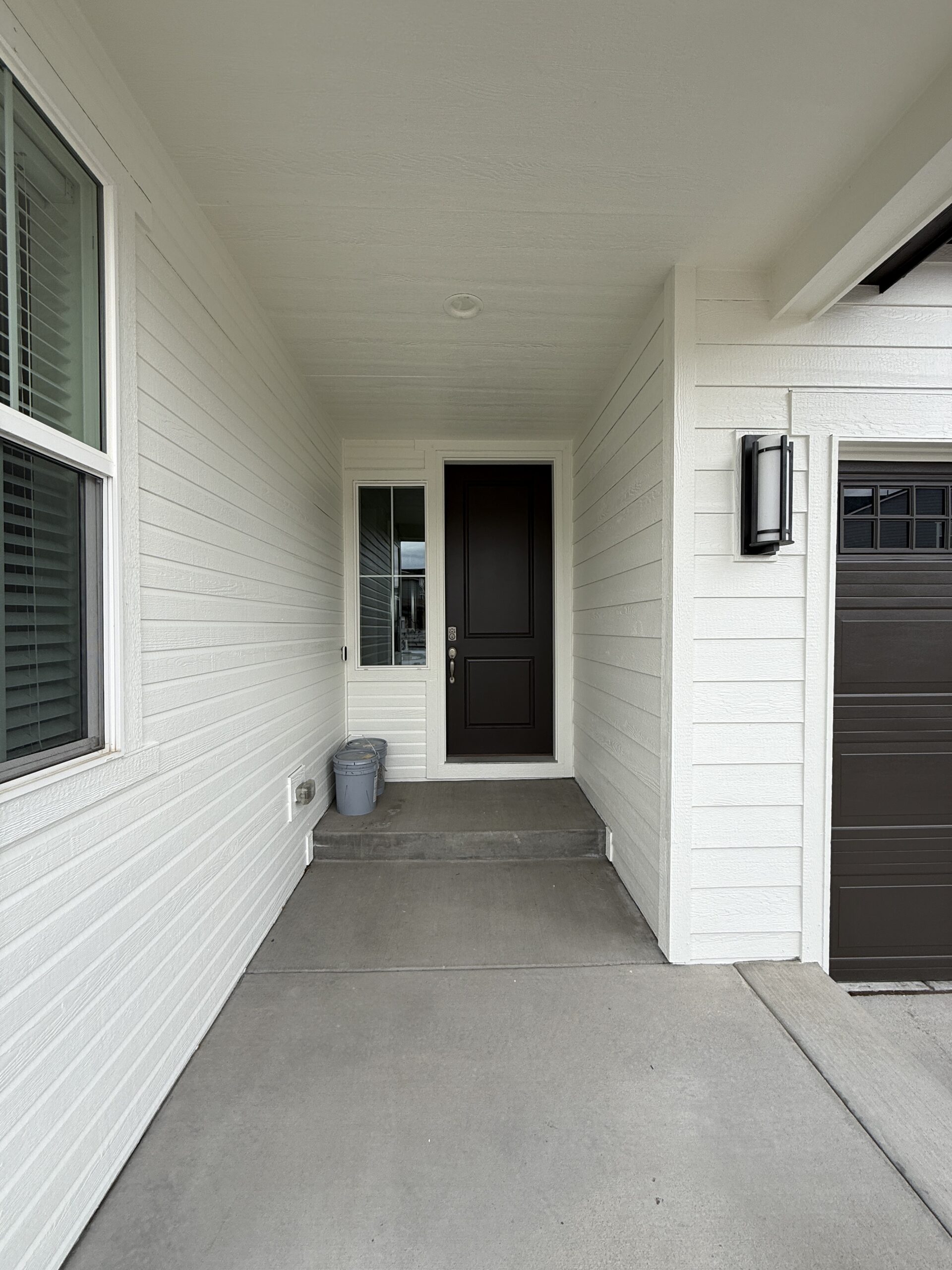Welcoming Home Entrance with Fresh White Exterior Paint A clean residential home entrance featuring white siding, a dark brown front door, and a matching garage.